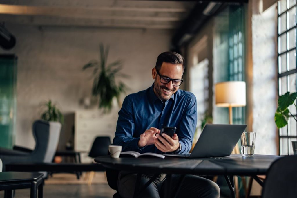 man looking at mobile phone while in front of laptop