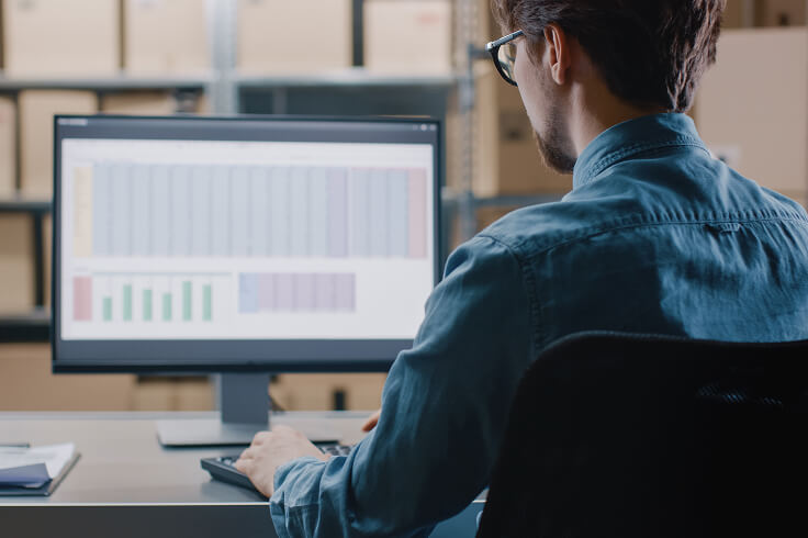 man typing on a desktop computer with a spreadsheet onscreen