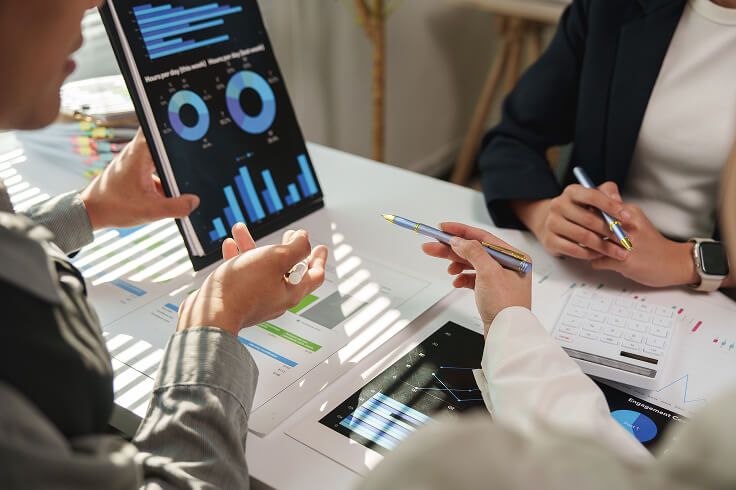 Several persons seen around a table viewing charts on a tablet