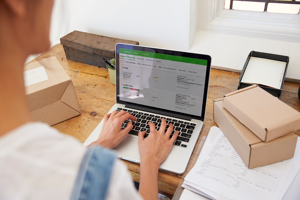 Someone typing on a computer on a desk with multiple brown boxes and loose paper