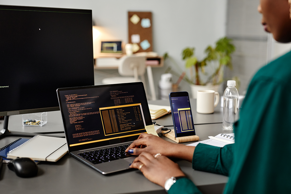 Female in a dark green blouse typing on a laptop with a tablet and large monitor